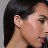 Close-up of a woman wearing a diamond earring against a neutral background