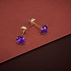 Gold earrings with purple gemstones on a red surface