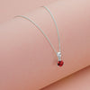 Silver necklace with a red gemstone pendant on a pink background