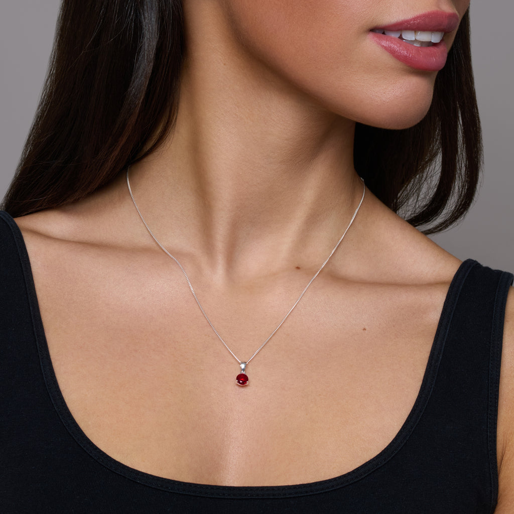 Silver necklace with a red gemstone pendant on a white background