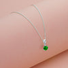 Silver necklace with a green gemstone pendant on a pink background