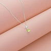 Silver necklace with a yellow gemstone pendant on a pink surface