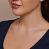Close-up of a woman wearing a silver necklace with a pendant against a neutral background