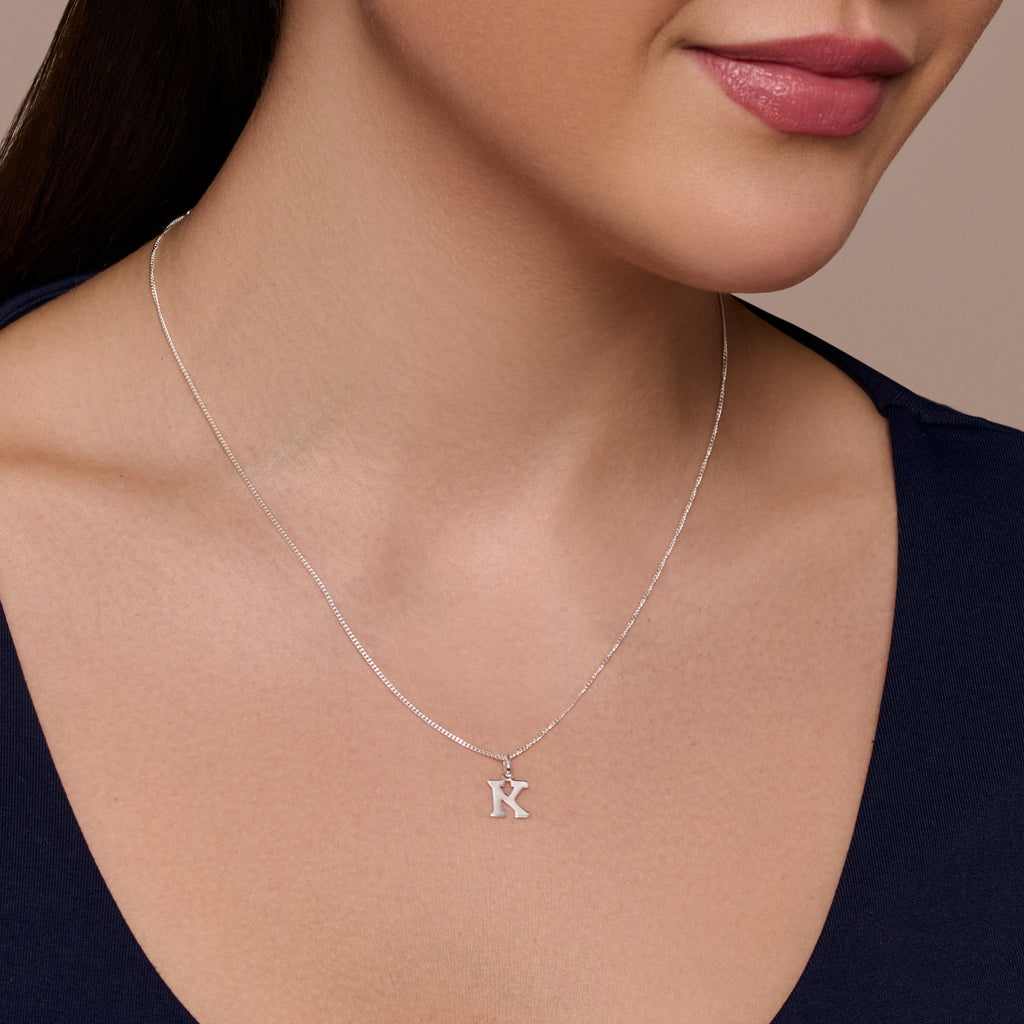 A sterling silver necklace with a large letter 'K' pendant on a chain.