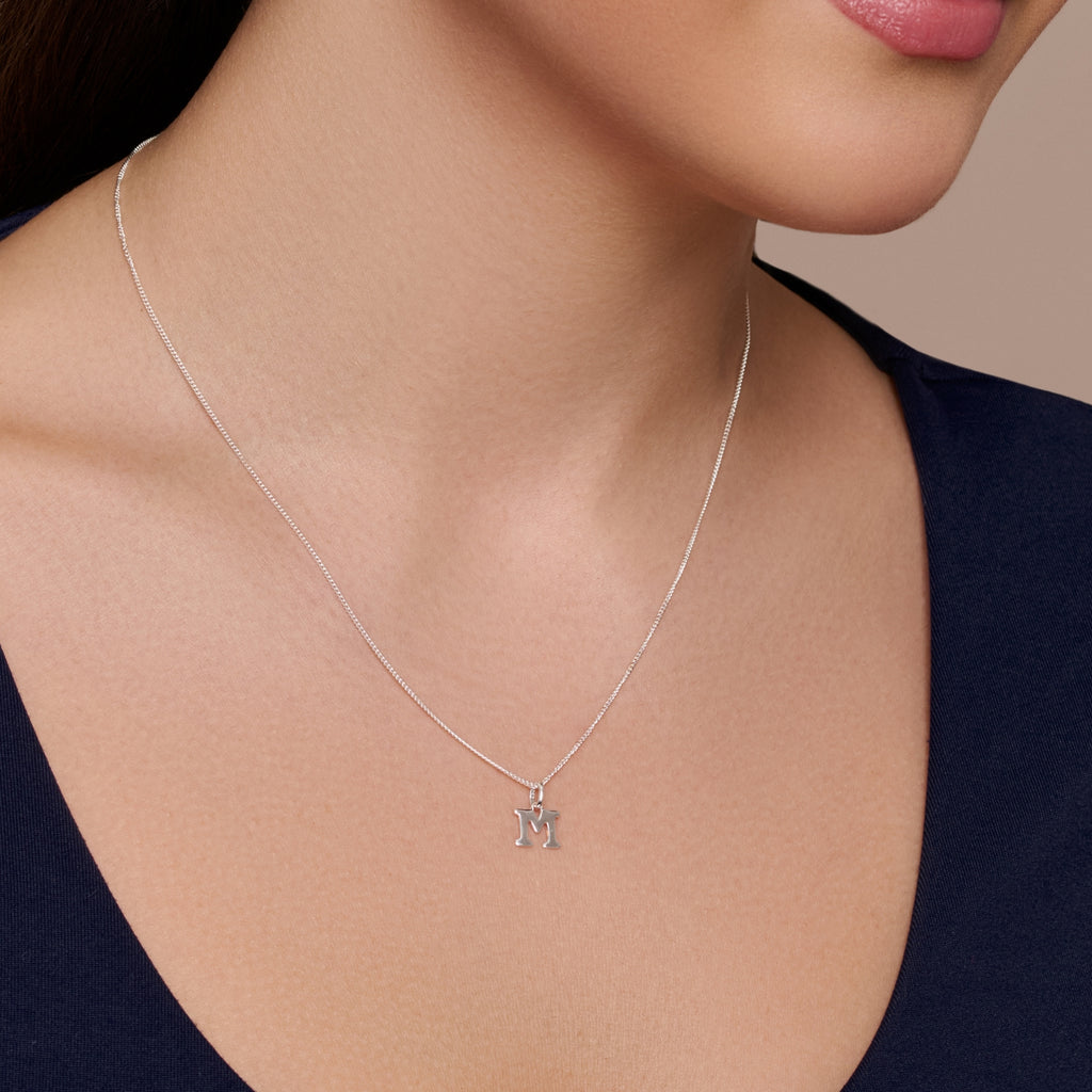 A sterling silver necklace pendant with the letter 'M' engraved in a clear, shiny finish on a chain.